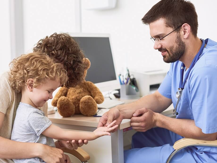 Arzt untersucht kleines Kind auf dem Schoß der Mutter